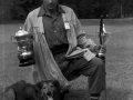 Pastor con su perro sosteniendo unos trofeos