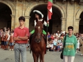 Niña montada a caballo durante los actos del Día del Niño. Se encuentra en la plaza de los Fueros, flanqueada por otras dos personas