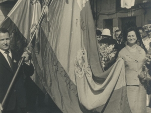 Momento del desfile en el que dos personas llevan una de las banderas ganadas