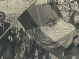 Momento del desfile en el que dos jóvenes llevan una de las banderas ganadas hacia la iglesia San Juan Bautista