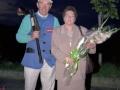 Pareja: el hombre porta una escopeta para practicar el tiro al plato y la mujer un ramo de flores